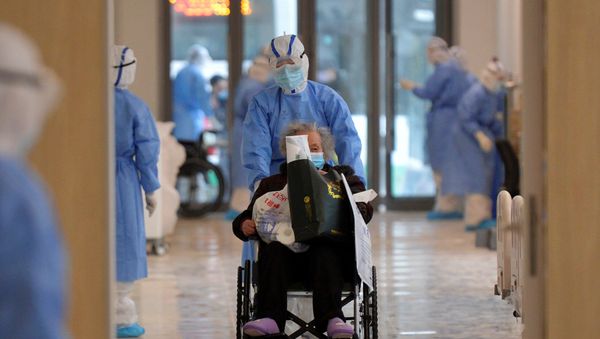 A medical worker in protective suit moves a novel coronavirus patient in a wheelchair at a hospital in Wuhan - Sputnik International