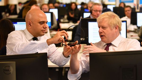 In this file photo taken on December 08, 2019 Britain's Chancellor of the Exchequer Sajid Javid (L) passes a headset to Britain's Prime Minister Boris Johnson (R) so that he can speak to a supporter as they man the phones at the Conservative Campaign Headquarters Call Centre in central London on December 8, 2019. In this file photo taken on December 08, 2019 Britain's Chancellor of the Exchequer Sajid Javid (L) passes a headset to Britain's Prime Minister Boris Johnson (R) so that he can speak to a supporter as they man the phones at the Conservative Campaign Headquarters Call Centre in central London on December 8, 2019. - Sputnik International