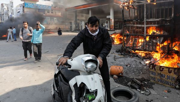 A man pushes his damaged scooter past a burning petrol pump during a clash between people supporting a new citizenship law and those opposing it, in New Delhi India, February 24, 2020 - Sputnik International