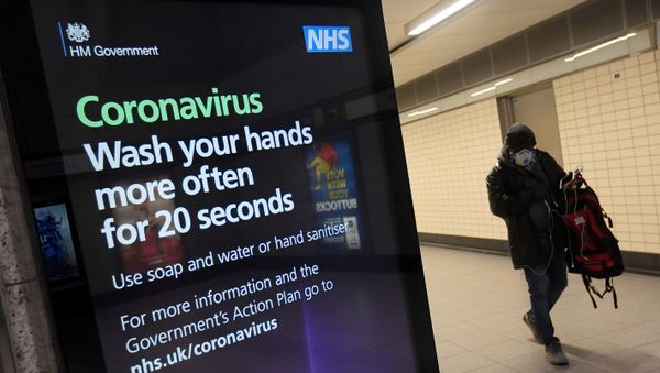 A man in a protective face mask walks past a British government public health campaign advertisement at Victoria underground station - Sputnik International