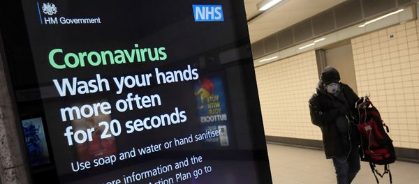 A man in a protective face mask walks past a British government public health campaign advertisement at Victoria underground station - Sputnik International