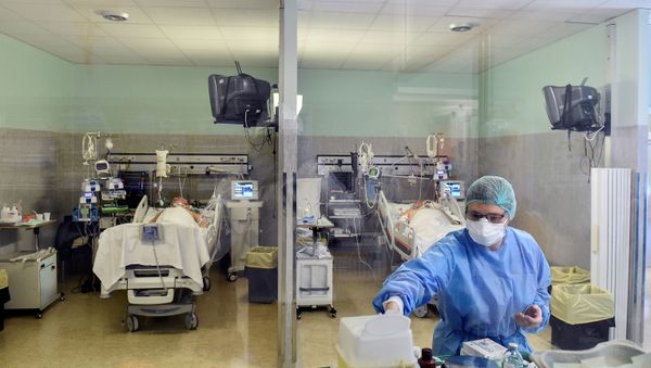 A medical worker wearing a protective mask and suit treats patients in Italy - Sputnik International