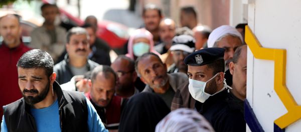 A policeman, wearing a mask as a precaution against the the coronavirus disease (COVID-19), stands guard as Palestinians wait outside a bank to withdraw cash, in Gaza City 29 March 2020. - Sputnik International