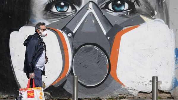 A man wearing a face mask walks past a graffiti A man wearing a face mask walks past a graffiti - Sputnik International
