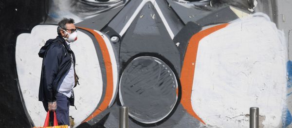 A man wearing a face mask walks past a graffiti A man wearing a face mask walks past a graffiti - Sputnik International