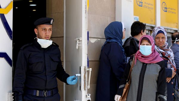 A Palestinian policeman stands guard as a woman, wearing a mask as a precaution against the the coronavirus disease (COVID-19), waits with other people outside a bank to withdraw cash, in Gaza City March 29, 2020 A Palestinian policeman stands guard as a woman, wearing a mask as a precaution against the the coronavirus disease (COVID-19), waits with other people outside a bank to withdraw cash, in Gaza City March 29, 2020 - Sputnik International
