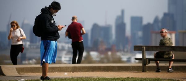 A man wearing a face mask looks at his phone on Primrose Hill in London - Sputnik International