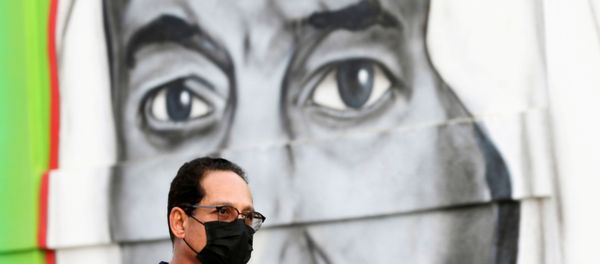 A Saudi man walks past a poster depicting Saudi King Salman bin Abdulaziz, after a curfew was imposed to prevent the spread of the coronavirus disease (COVID-19), in Riyadh, Saudi Arabia March 25, 2020 - Sputnik International