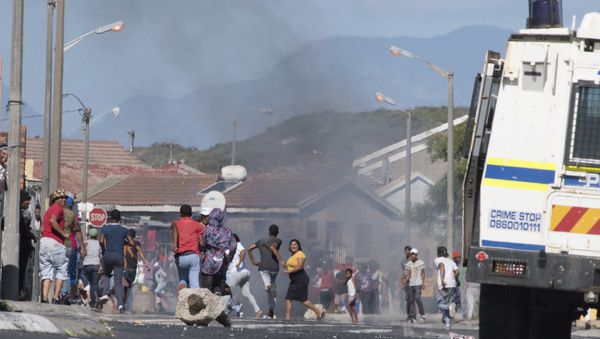 People run away as a South African Police Services armoured vehicle drives into a street during clashes with residents of Tafelsig, an impoverished suburb in Mitchells Plain, near Cape Town, on April 14, 2020, after some people in the community did not receive food parcels which were being handed out as part of the support for this community during the nation wide lockdown to curb the spread of the COVID-19 coronavirus.  - Sputnik International