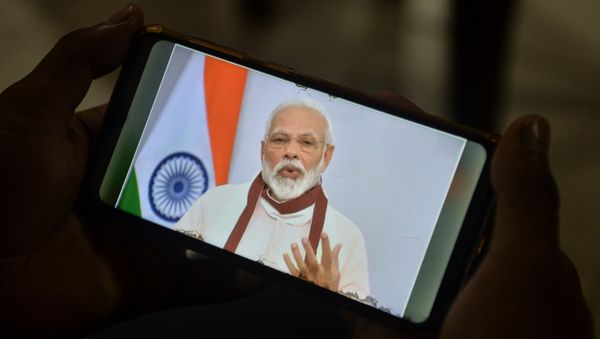 A youth watches Indian Prime Minister Narendra Modi's address to the nation on his mobile phone during a government-imposed nationwide lockdown as a preventive measure against the COVID-19 coronavirus, in Siliguri on 12 May 2020.  - Sputnik International