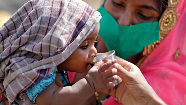 A child of a migrant worker drinks water as his mother holds him while waiting in a queue for transport to reach to a railway station to board a train to their home state of northern Uttar Pradesh, after a limited reopening of India's giant rail network following a nearly seven-week lockdown to slow the spreading of the coronavirus disease (COVID-19), in Ahmedabad, India, May 15, 2020 - Sputnik International