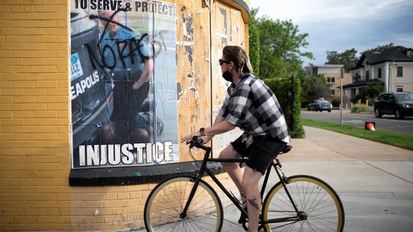 A cyclist passes a poster showing former Minneapolis police officer Derek Chauvin kneeling on George Floyd - Sputnik International