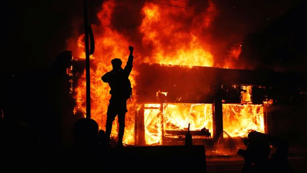 A protester gestures as buildings burn during continued demonstrations against the death in Minneapolis police custody of African-American man George Floyd, in Minneapolis, Minnesota, U.S., May 30, 2020 A protester gestures as buildings burn during continued demonstrations against the death in Minneapolis police custody of African-American man George Floyd, in Minneapolis, Minnesota, U.S., May 30, 2020 - Sputnik International