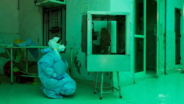 A medical worker wearing Personal Protective Equipment (PPE) relaxes in front of an air cooler - Sputnik International
