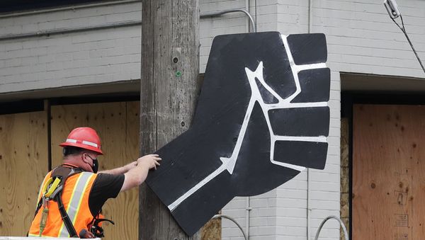 A worker removes a rendering of a clenched fist from a Seattle police precinct Wednesday, July 1, 2020, in Seattle, where streets had been blocked off in an area demonstrators had occupied for weeks. Seattle police showed up in force earlier in the day at the occupied protest zone, tore down demonstrators' tents and used bicycles to herd the protesters after the mayor ordered the area cleared following two fatal shootings in less than two weeks. The Capitol Hill Occupied Protest zone was set up near downtown following the death of George Floyd while in police custody in Minneapolis. - Sputnik International