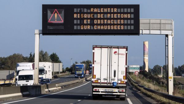 This picture taken on October 13, 2016 shows a truck driving under a board reading Slow down, possible pedestrians and obstacles on the road, on the circular road next to the Jungle migrant camp in Calais, northen France. - French authorities prepare to raze the Calais Jungle camp and move thousands of migrants to shelters nationwide. Two towns a few kilometres apart in the countryside near Paris reveal a nation torn between fear and fraternity. - Sputnik International
