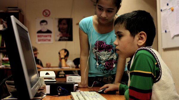 At a refugee school in Moscow, two children play on a computer, while other students are tutored by volunteer teachers. - Sputnik International